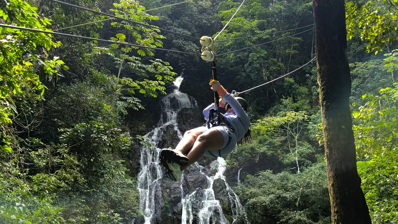 Person riding a zipline in front of a waterfall surrounded by forest